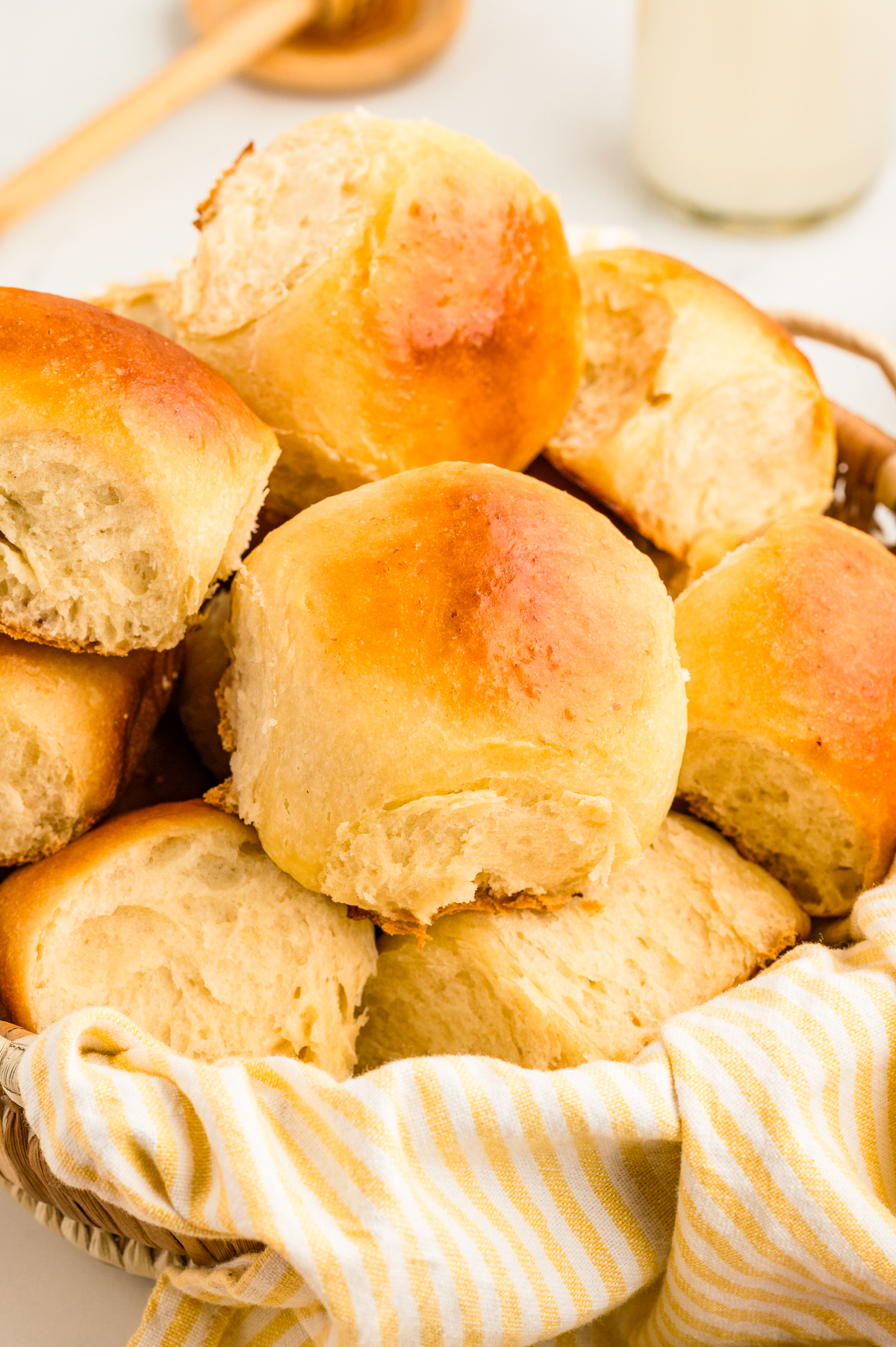 A dozen of dinner rolls in a basket with a stripped yellow dish towel. 